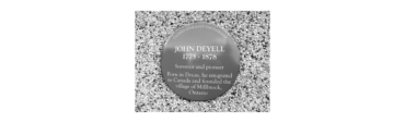 Circular commemorative plaque on gravel: 'John Deyell 1775–1878' with text about a surveyor and pioneer and the village of Millbrook, Ontario.