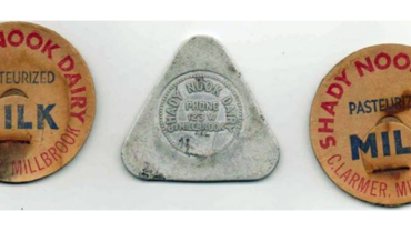 Three dairy bottle caps: two orange round lids reading 'Shady Nook Dairy' and 'Milk' with 'Pasteurized' text, flanking a silver triangular cap in the center.
