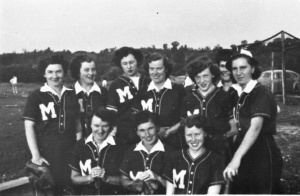 Group of women in matching baseball/softball uniforms with a large 'M' on the chest, posing outdoors on a field.