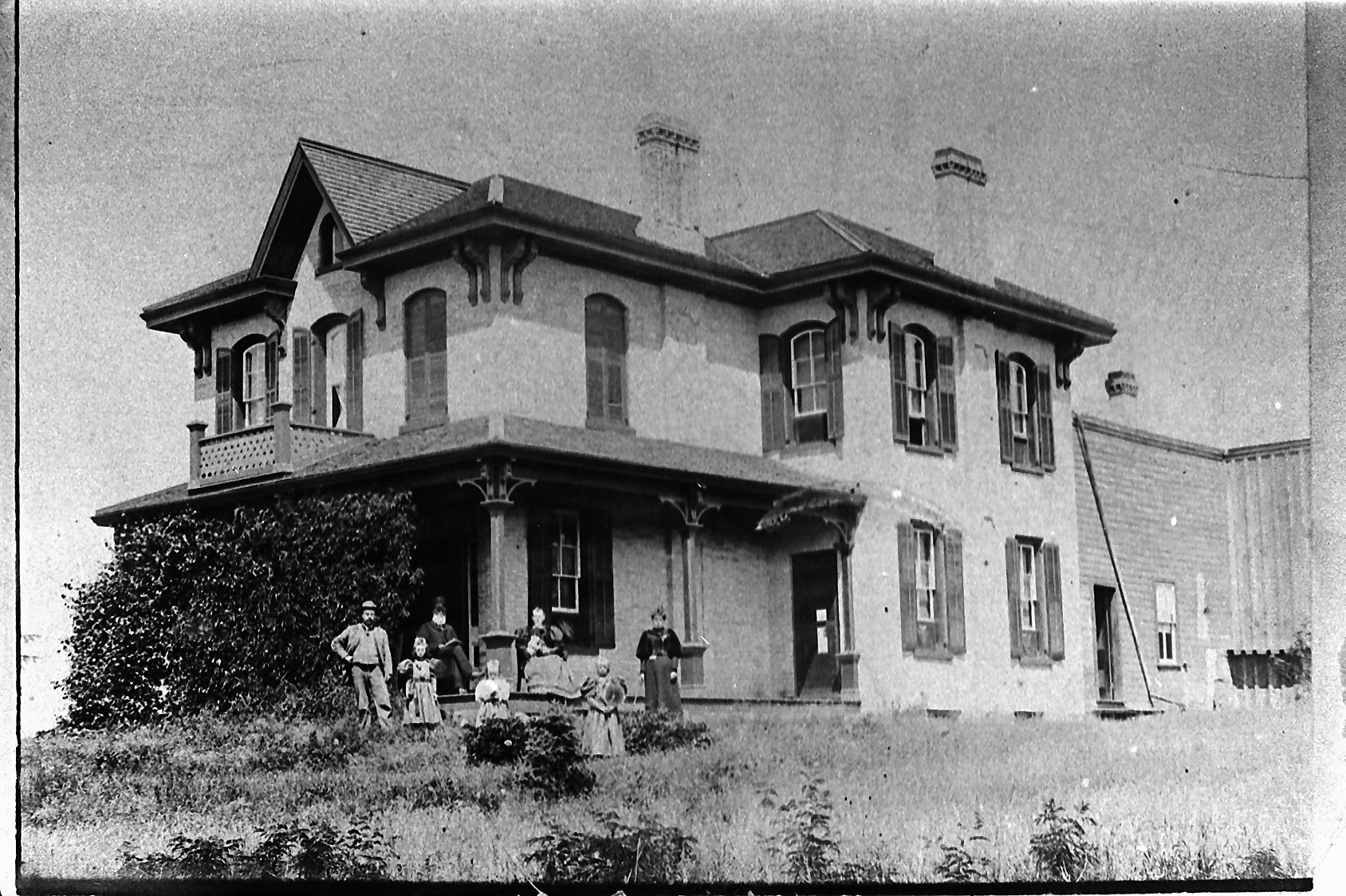 Two-story Victorian-style house with ornate brackets; family stands on the front lawn.