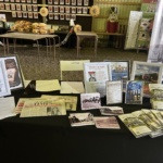 Informational display booth with framed posters, newspapers, and photos about local history at a museum exhibit.